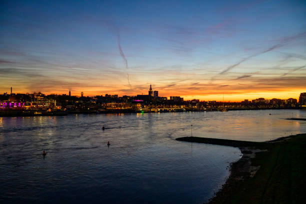 Skyline of the city Nijmegen on the riverbank of the Waal seen from the Waalbrug during sunset. Various ships are passing the river during this beautiful cold winter sunset during the blue hour at the end of the day.