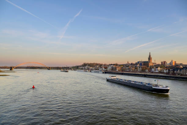 Skyline of the city Nijmegen on the riverbank of the Waal seen from the Waalbrug during sunset. Various ships are passing the river during this beautiful cold winter sunset during the blue hour at the end of the day.