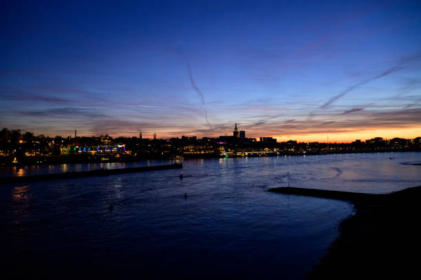 Skyline of the city Nijmegen on the riverbank of the Waal seen from the Waalbrug during sunset. Various ships are passing the river during this beautiful cold winter sunset during the blue hour at the end of the day.