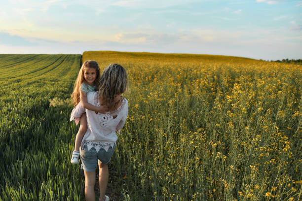 Young mother and daughter in field on a sunset. Single mother is carrying little girl.
