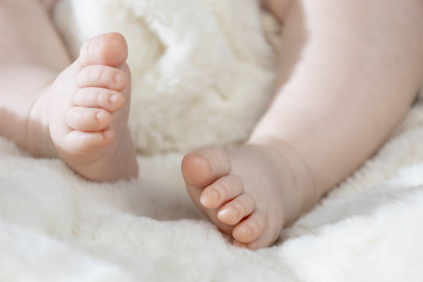 Legs infant baby lying on white bed.