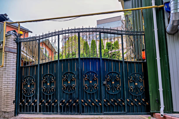 A black wrought iron gate with decorative elements set against a backdrop of buildings and a clear sky