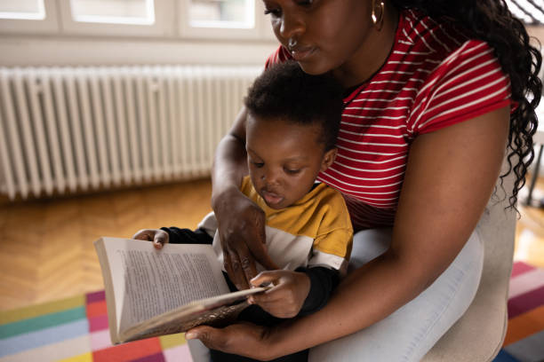 Mother with son reading book, sitting on floor, laughing