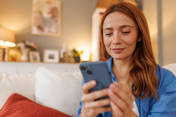 istock Young woman using mobile phone sitting on sofa at home 2194857065