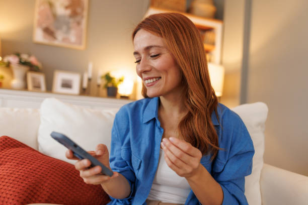 istock Happy young woman using remote control, watching tv on sofa at home 2194857132
