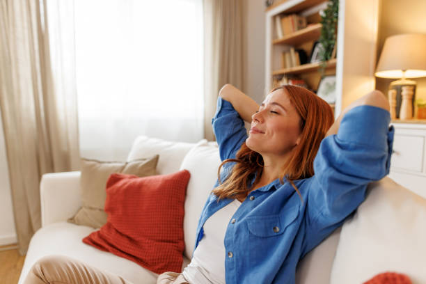 young woman relaxing on sofa with hands behind head - confortável - fotografias e filmes do acervo