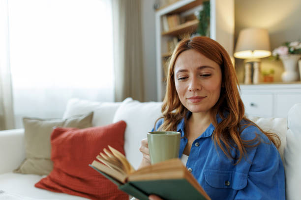 istock Young woman relaxing on sofa reading book and drinking tea 2194857940