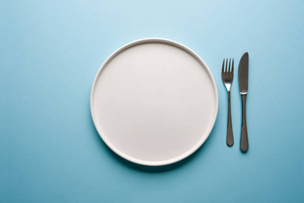 istock Top view of empty ceramic white plate and cutlery on blue background 2194862589