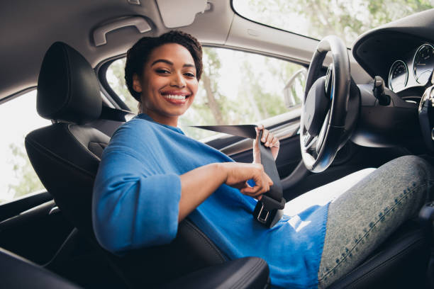 istock Young woman smiling confidently while buckling seatbelt inside car, ready for a summer urban drive, wearing casual style on a bright day 2194862903