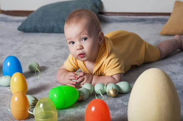 istock Baby in Yellow Outfit Playing with Colorful Easter Eggs on a Soft Carpet 2194865334