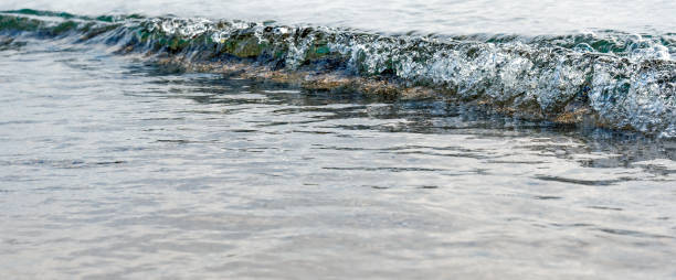 istock Shining silvery surface of a calm sea, a wave rolling onto a sandy shore 2194865988