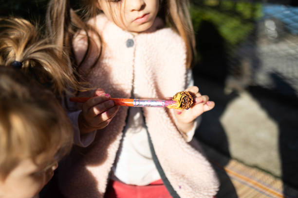 The girl is holding a pine cone and painting it with yellow watercolor.