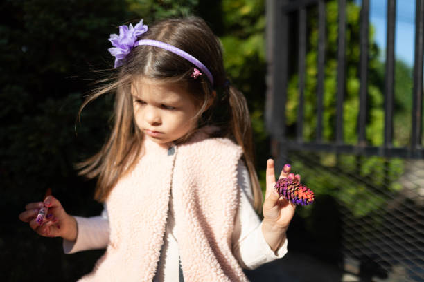 The little girl is painting the pine cone in the backyard with some water colors.
