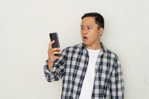 istock Young Asian man pointing to mobile phone with afraid and surprised expression. Promo and bad news concept 2194873344