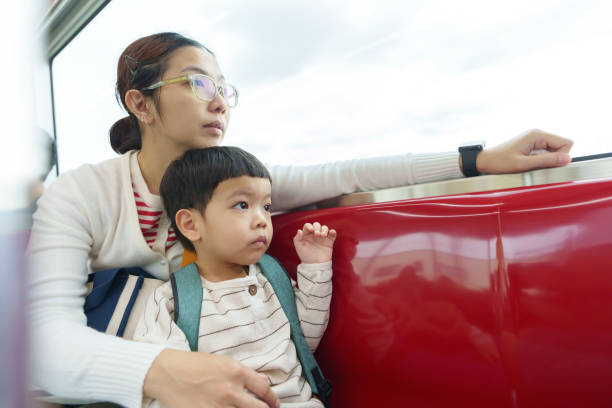 istock Mother holding her son while sitting on a red train seat, both looking outside during a daytime ride. 2194874664