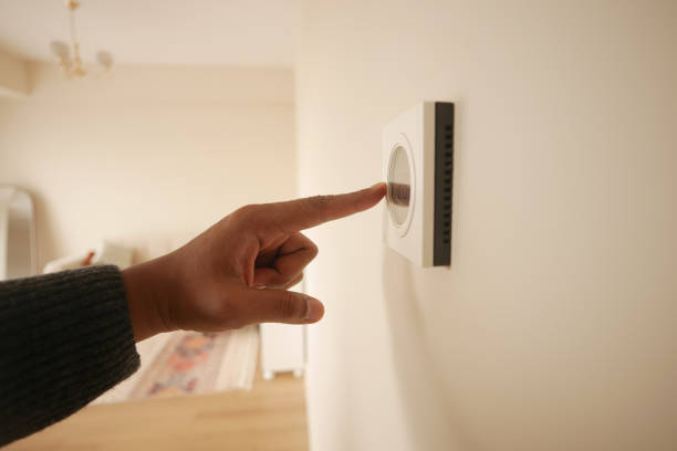 istock Hand Adjusting Smart Thermostat on White Wall for Optimal Home Temperature Control 2194875585