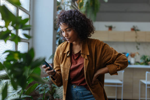 istock Young woman using smartphone next to a window in her apartment 2194875737