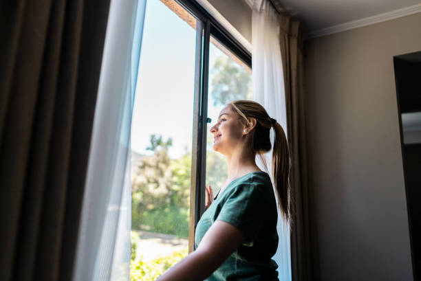 istock Young woman looking through window at home 2194878776