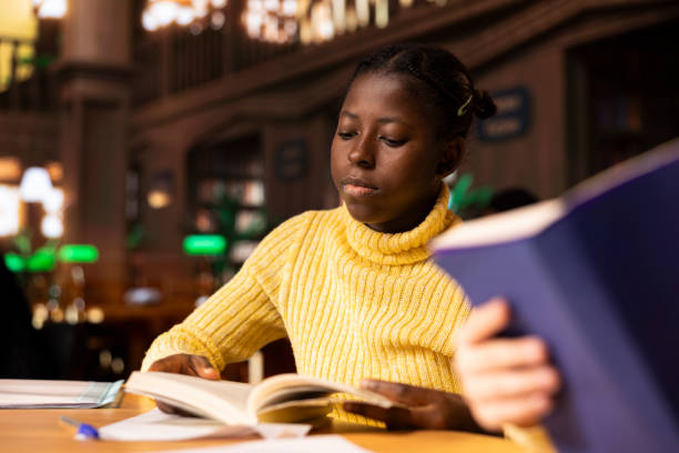 istock Black schoolgirl studying in a public library reading required literature 2194888143