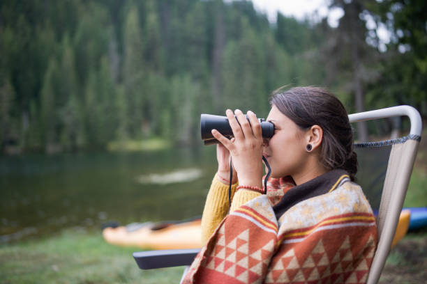Enjoying her peaceful vacation, a woman watches the distant landscape through binoculars while surrounded by the calm of the outdoors.