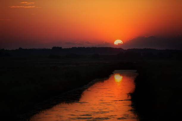 Beautiful orange sunset over a narrow river. Calm natural evening scene.