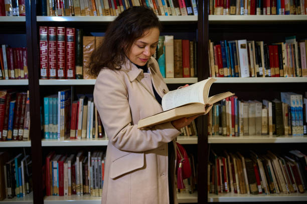 istock Woman enjoying reading a book in a library surrounded by shelves 2194890376