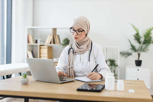istock Muslim female doctor conducts patient video call using laptop and taking notes 2194893336