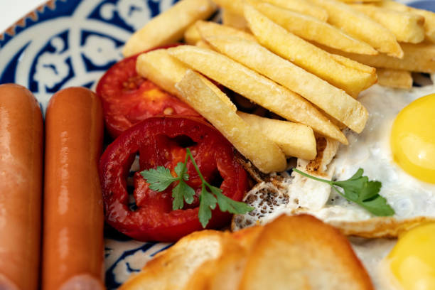 Breakfast plate with fried eggs, sausage, tomatoes, and fries served on a decorative blue plate close up