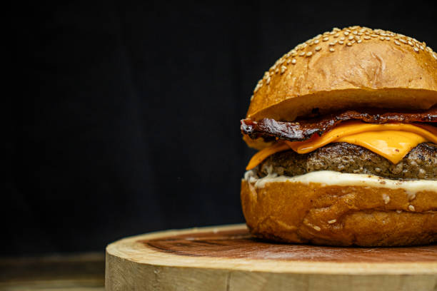 istock Artisanal burger with white sauce, cheddar, and bacon on wooden base, dark background 2194895088