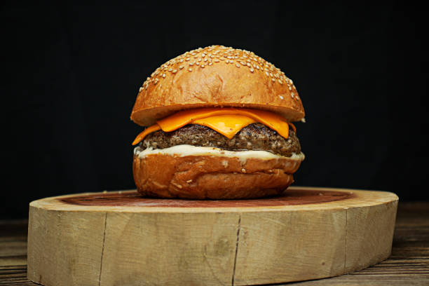 istock Artisanal burger with white sauce, cheddar on wooden base, dark background 2194895103