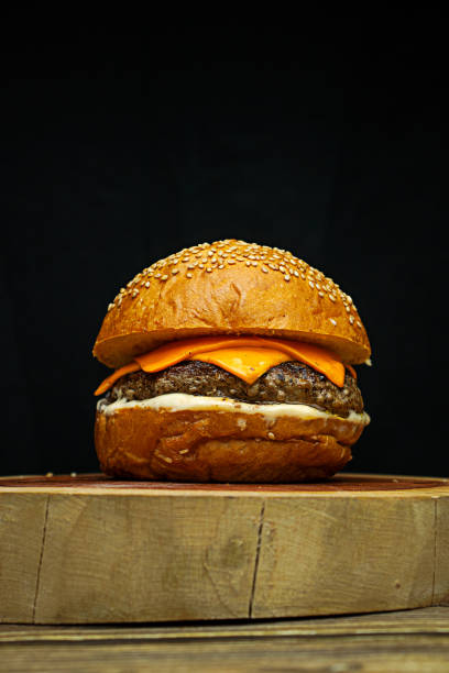 istock Artisanal burger with white sauce, cheddar on wooden base, dark background 2194895108