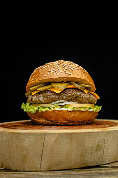 istock Artisan hamburger with white sauce, cheddar cheese, pickles, lettuce, onion and tomato on a wooden base. 2194895507