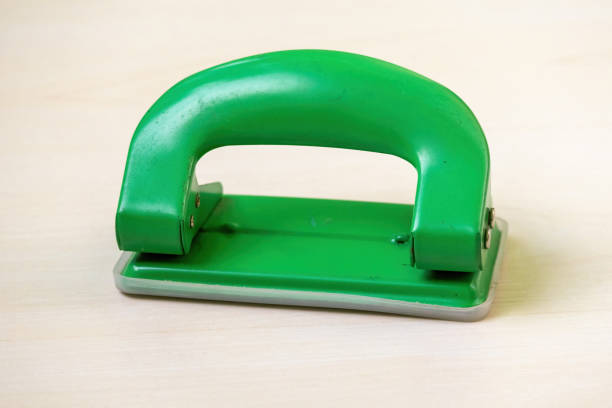 A green paper hole puncher or punch machine on a light wooden surface.