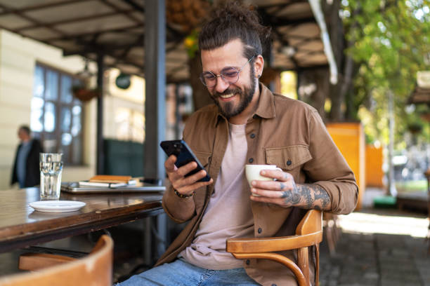 istock Young man drinking coffee and using phone in a sidewalk cafe 2194897221