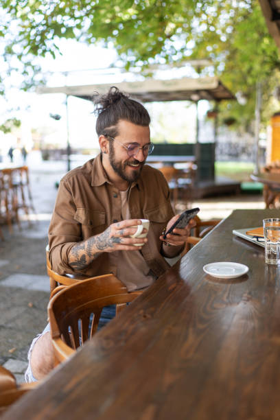 istock Young man drinking coffee and using phone in a sidewalk cafe 2194897267