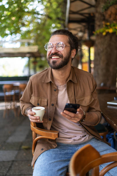istock Young man drinking coffee and using phone in a sidewalk cafe 2194897482