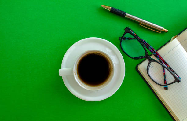Glasses, notepad, pen and coffee cup on a green background, top view. Mockup diary. Business, freelancing, back to school.