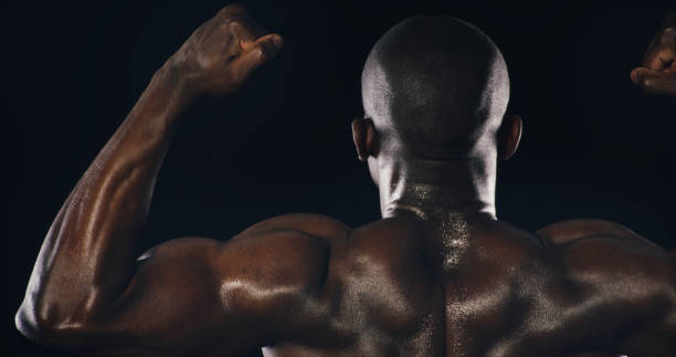 istock Flexing, muscles and back of black man in studio with sweating for bodybuilding workout. Fitness, strength and African male athlete with sports exercise, challenge or training by black background. 2194906490