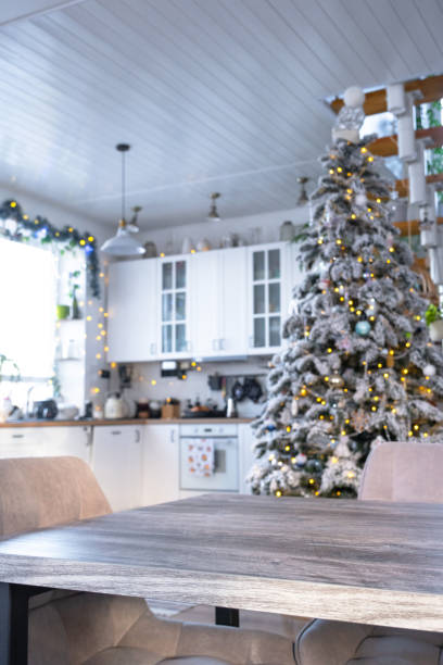 istock Grey Wooden empty table to demonstrate product with space for text with upholstered chairs in white kitchen, modern interior with Christmas tree and fairy lights. New Year, Christmas mood, cozy home. 2194910108