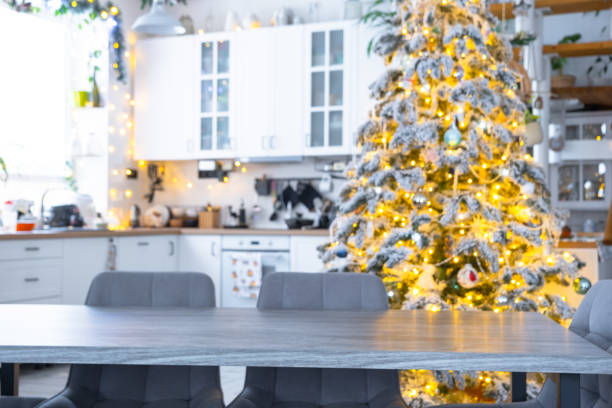 istock Grey Wooden empty table to demonstrate product with space for text with upholstered chairs in white kitchen, modern interior with Christmas tree and fairy lights. New Year, Christmas mood, cozy home. 2194910110