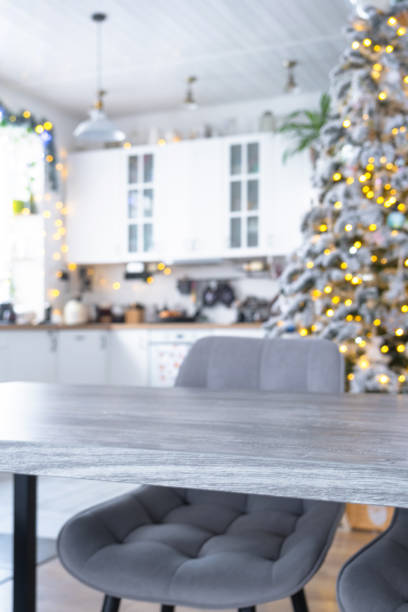 istock Grey Wooden empty table to demonstrate product with space for text with upholstered chairs in white kitchen, modern interior with Christmas tree and fairy lights. New Year, Christmas mood, cozy home. 2194910117
