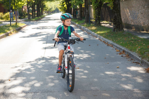 Boy with cycling helmet going to school on his bike, riding through suburb. With backpack ready for scool.