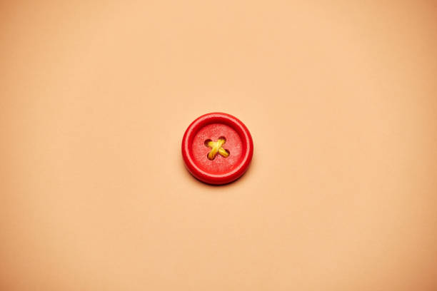 One alone red clothes sewing button with a yellow rope cross isolated on the bright solid fond plain sandy beige background