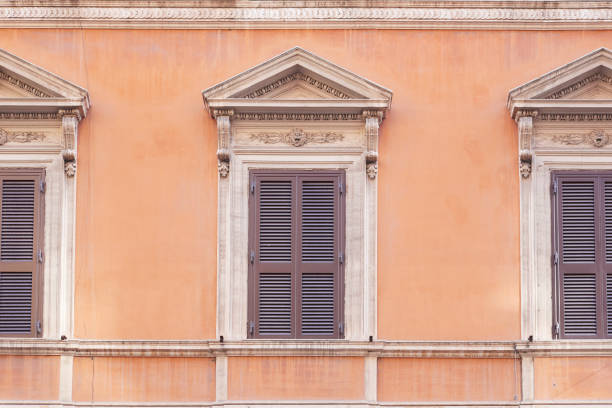 Old wooden window with shutters on an orange wall in Rome, Italy