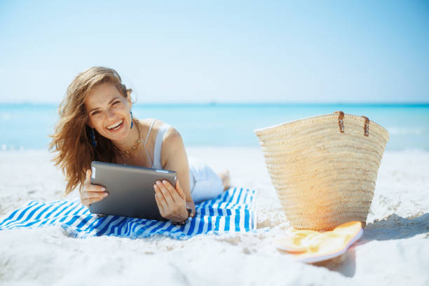 smiling stylish woman on ocean shore using app on tablet PC stock photo