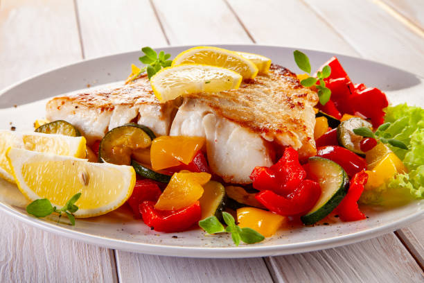 istock Fish dish - fried cod fillet with fried vegetables and lemon served on wooden table 2194923285