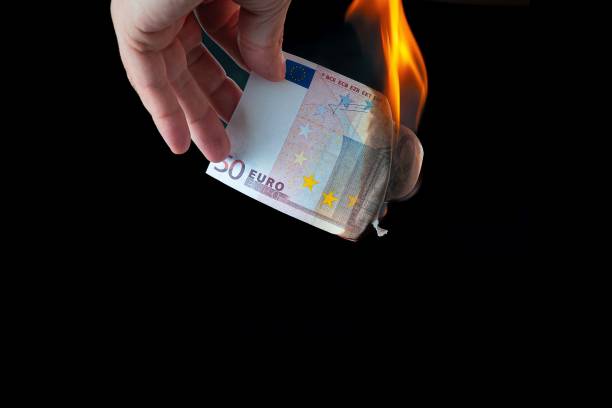 istock 50 Euro note held by a hand while it burns due to the flame of a lighter with a black background 2194927733