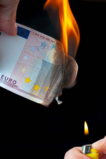 istock 50 Euro note held by a hand while it burns due to the flame of a lighter with a black background 2194927739
