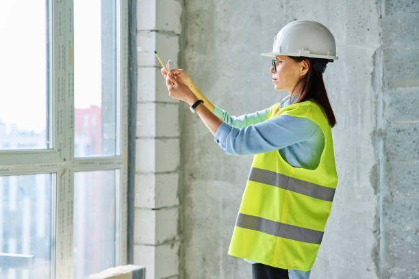 istock Female industrial worker in protective vest helmet using smartphone at construction site 2194931566