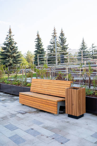 istock In a serene park setting, a sturdy wooden bench is positioned conveniently beside a trash can, creating a practical yet inviting space for park visitors to rest and enjoy the scenery 2194932905